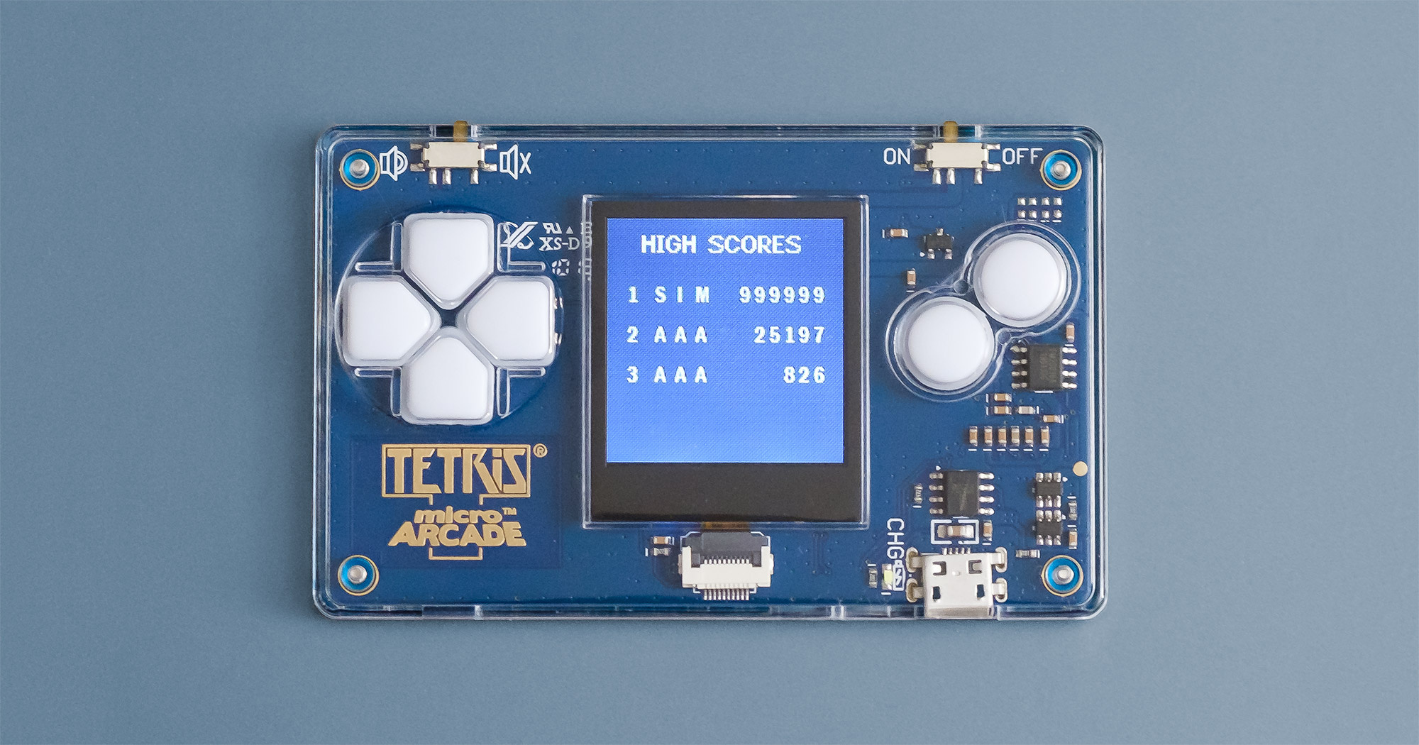 The Tiny Arcade Tetris device laying flat on a surface with the highscores screen showing. The screen shows the title 'High Scores' and lists the following three scores: 1 SIM 999999, 2 AAA 25197, 3 AAA 826.